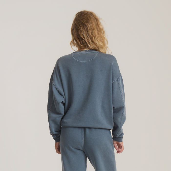 Woman wearing slate blue Made To Fade fleece hoodie with matching joggers, photographed from behind against neutral background