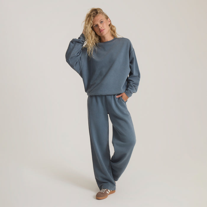 Woman wearing slate blue fleece crewneck sweatshirt and matching wide-leg sweatpants, standing against neutral background
