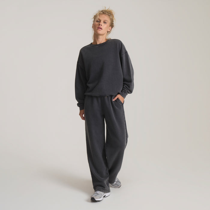 Woman wearing vintage black fleece sweatshirt and matching relaxed-fit sweatpants, styled with white sneakers on neutral background