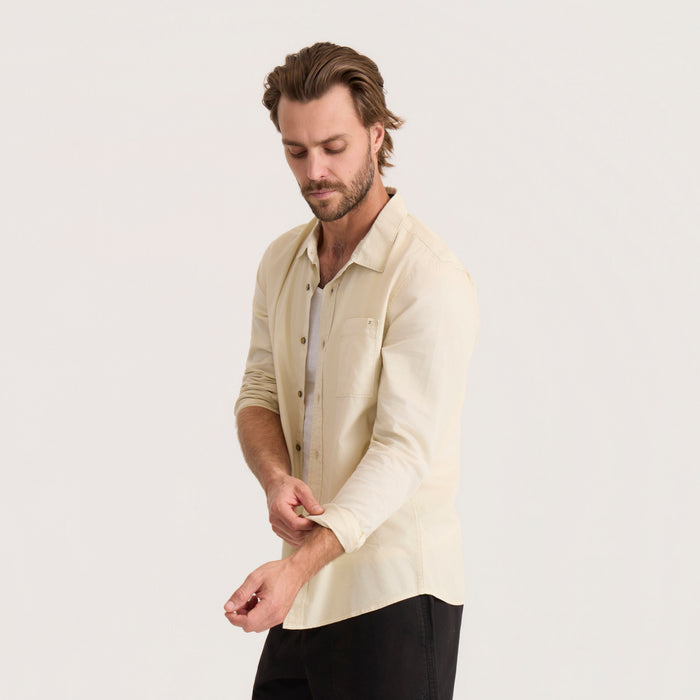 Man wearing washed bone long sleeve button up shirt with rolled sleeves and black pants against neutral background