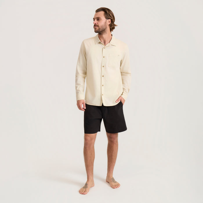 Man wearing washed bone long sleeve button up shirt with black shorts, standing against neutral background