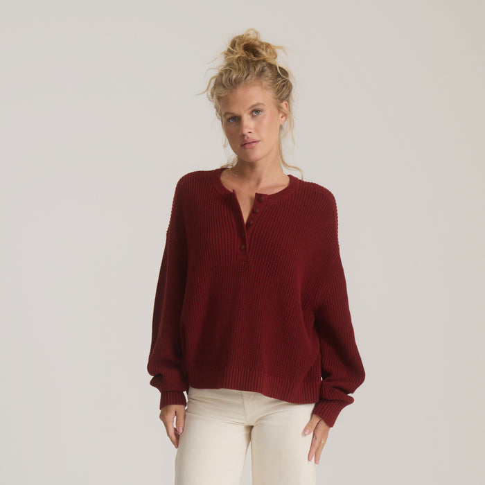 Made To Fade Sweater in cherrywood red ribbed knit with henley neckline, worn on model with cream pants