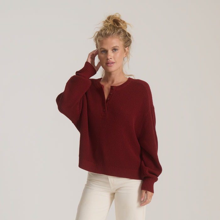 Deep burgundy ribbed sweater with long sleeves and notch neckline worn with cream pants on model