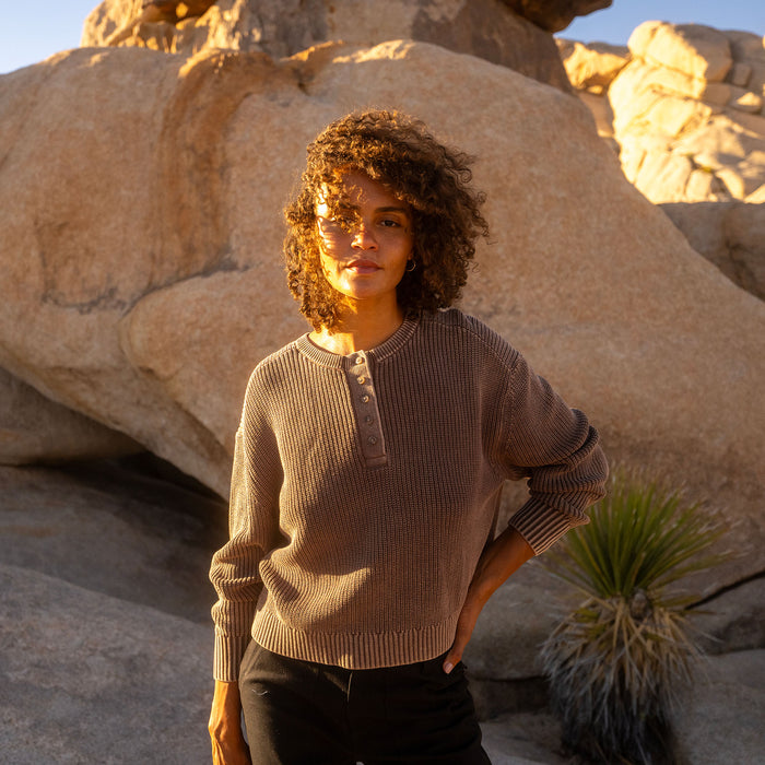 Coco Bean long sleeve sweater with henley neckline on model standing outdoors among large rocks at sunset