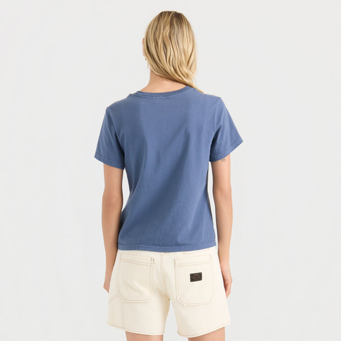 Woman wearing Neptune blue short-sleeve tee and cream denim shorts, shown from behind against white background