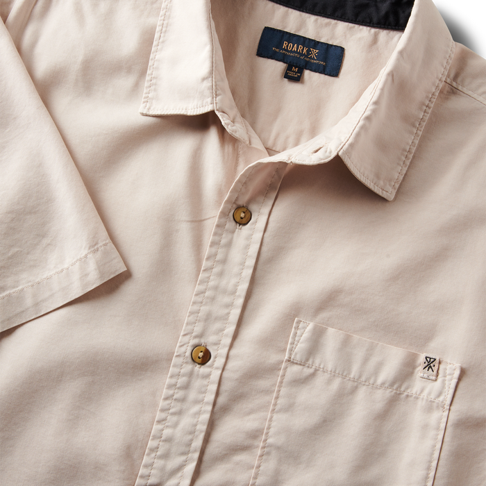Close-up of the Roark Made To Fade Short Sleeve Button Up Shirt's collar, buttons, and chest pocket with embroidered logo in Washed Bone.
