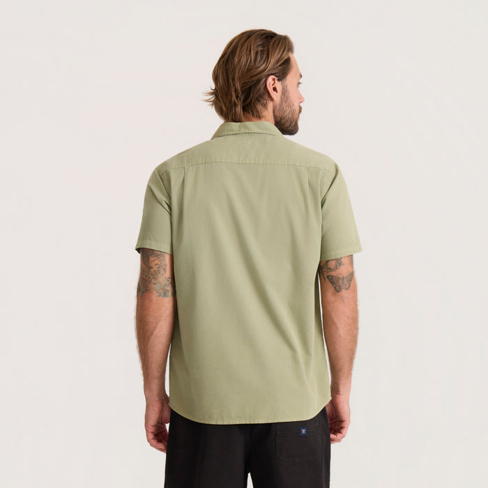 Man wearing sage green short sleeve button-up shirt, shown from behind against neutral background