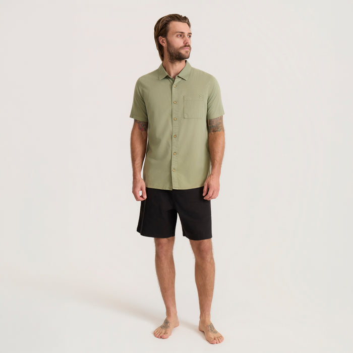 Sage green short sleeve button up shirt with chest pocket worn by man with black shorts in full body lifestyle shot