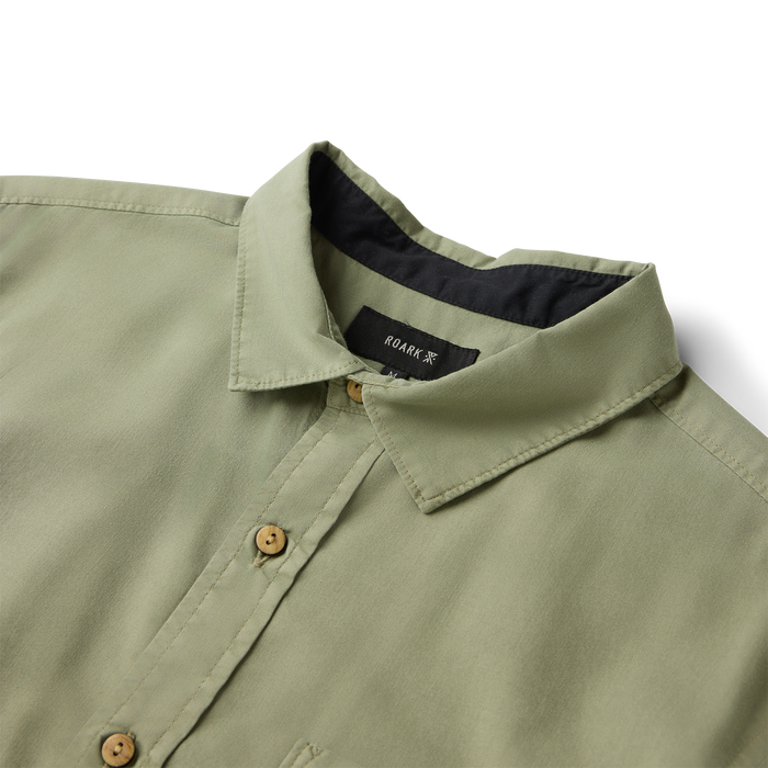 Sage green short sleeve button up shirt with wooden buttons and black interior lining visible at collar detail