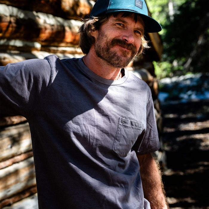 Man with a rugged beard wearing a Roark Made To Fade Tee and outdoor headgear, embodying adventure and exploration in nature.