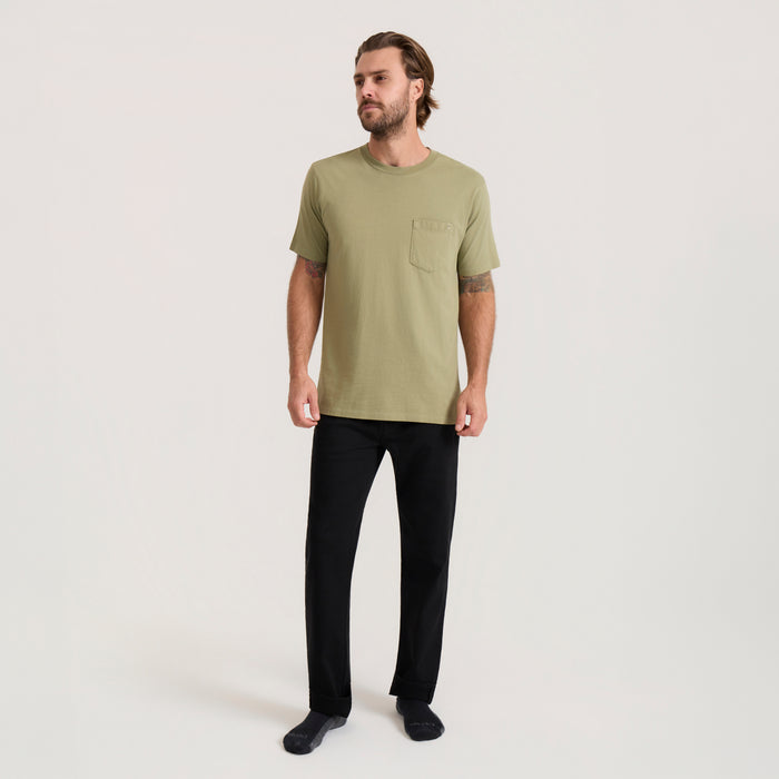 Man wearing washed dusty sage short sleeve tee with chest pocket and black pants, standing against neutral background