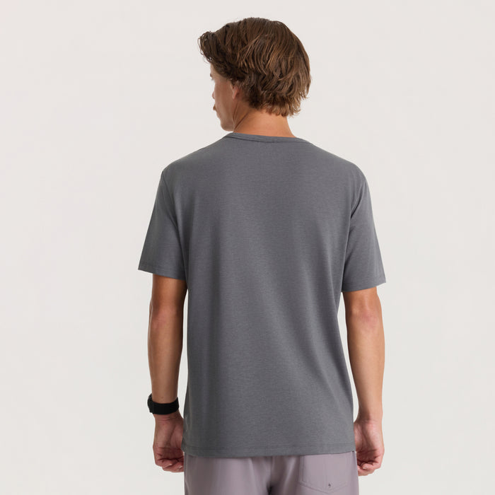 Charcoal gray short sleeve tee on male model shown from back, paired with light gray pants and black wristband