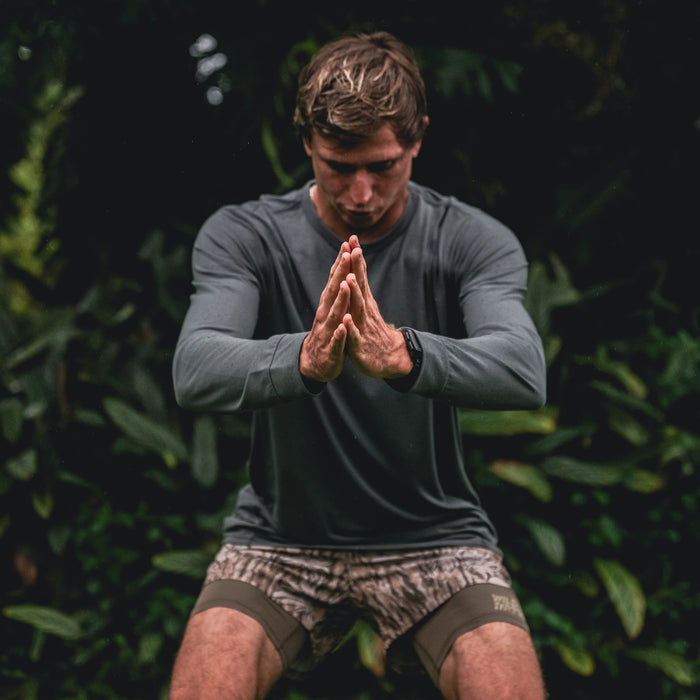 Active male wearing the Mathis Long Sleeve Tee by Roark, demonstrating flexibility and strength in sportswear designed for adventure and outdoor activities.