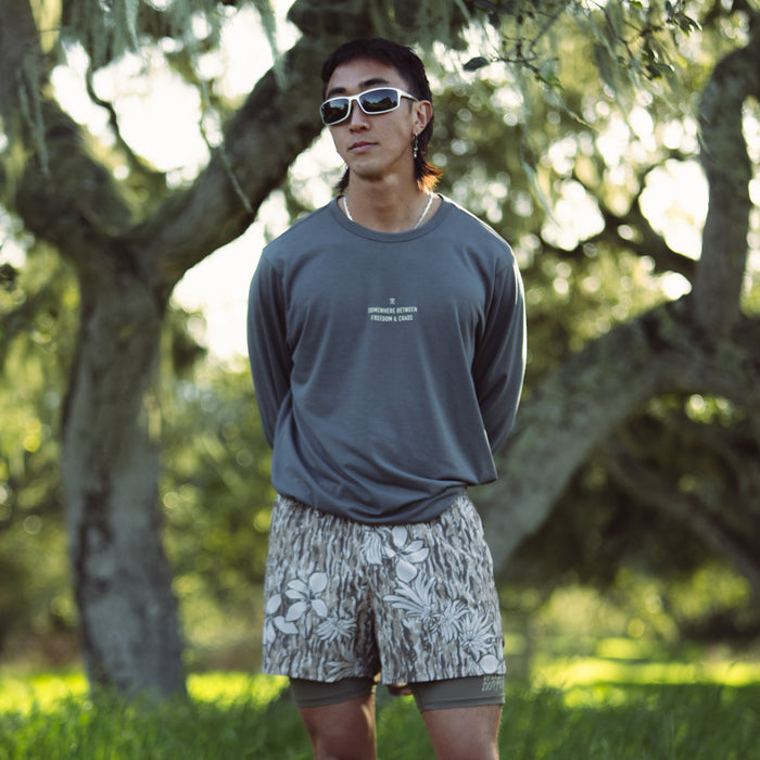 Athletic man wearing a Mathis Active Long Sleeve Tee paired with boardshorts, engaging in an outdoor adventure by the sea.