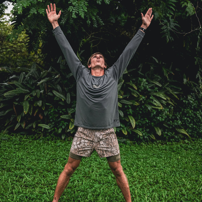 Happy person flexing muscles while wearing a green Mathis Active Long Sleeve Tee by Roark, enjoying nature