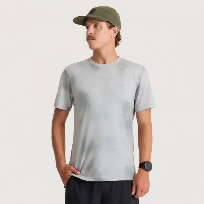 Man wearing light grey short-sleeve crew neck tee with small chest logo, paired with olive green baseball cap and black shorts