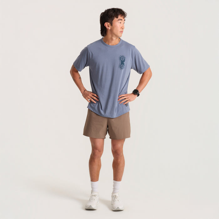 Active man standing in a natural setting, wearing Roark Bermuda shorts and a lightweight sleeve top, ready for adventure.
