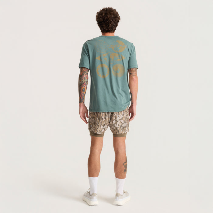 Man dressed in versatile Roark active shorts and shirt, equipped for adventure and outdoor activities, showcasing a streamlined fit for comfort and mobility.