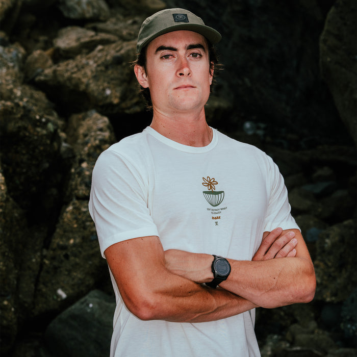 White Mathis Active graphic short sleeve tee on man wearing sage green cap, arms crossed, outdoors against rocky background