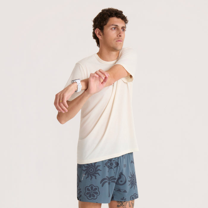 Man wearing unbleached cream short sleeve tee with blue patterned shorts and white wristband, standing against neutral background