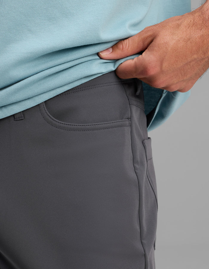 A close-up of a person wearing Cozy Earth's Men's Everywhere Pant - Relaxed Fit in gray, paired with a light blue shirt, as they lift the shirt slightly to reveal the pants' waistband.|Color:Graphite