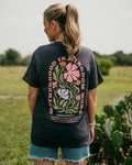 Person wearing a black t-shirt with floral design and text in an outdoor setting