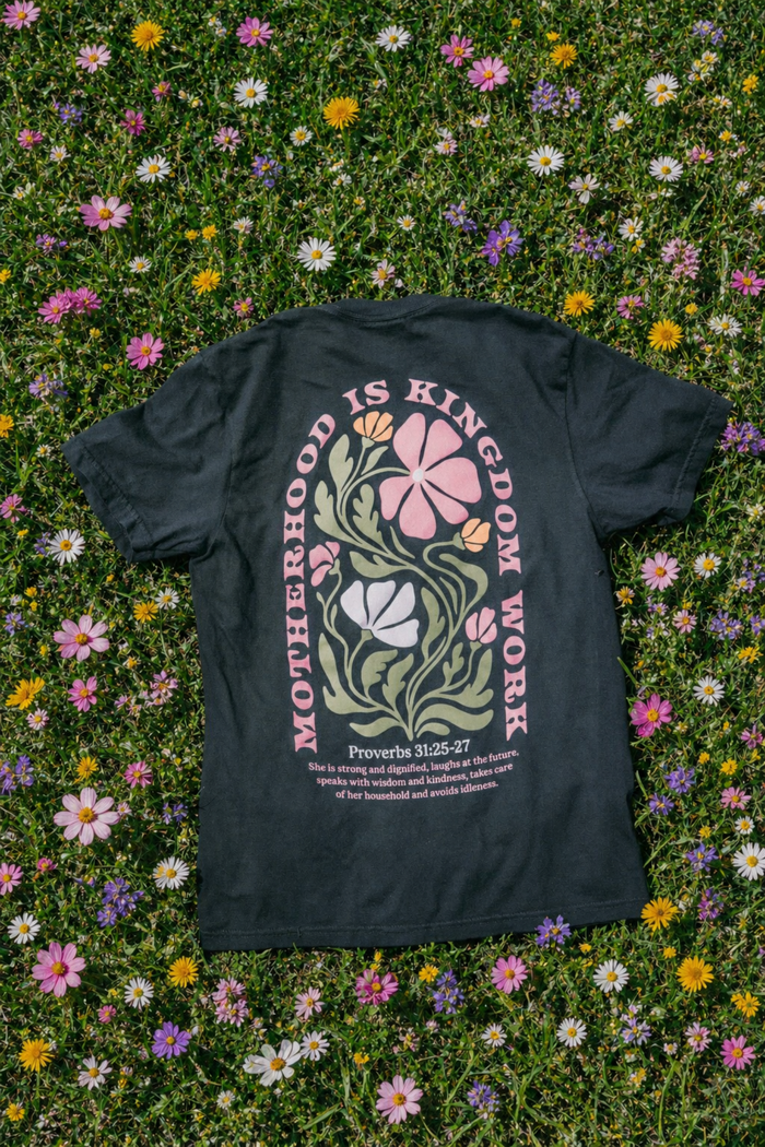 Black t-shirt with floral design and text on a grassy background with flowers