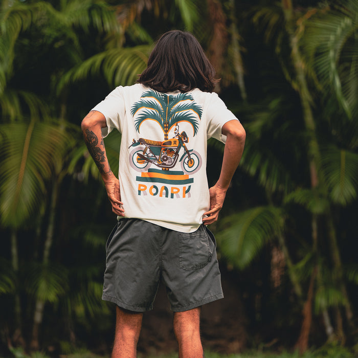 Man dressed in Roark Moto Palm Premium Tee and boardshorts, showcasing casual adventure-ready style with focus on sleeve and waist details.