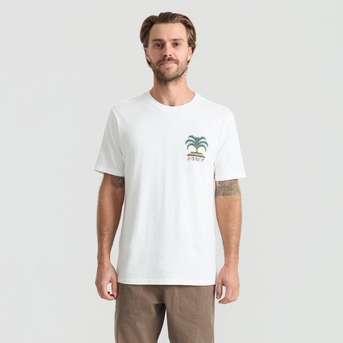 Active shirt by Roark framed by lush palm trees in a tropical setting, showcasing adventure and travel apparel.