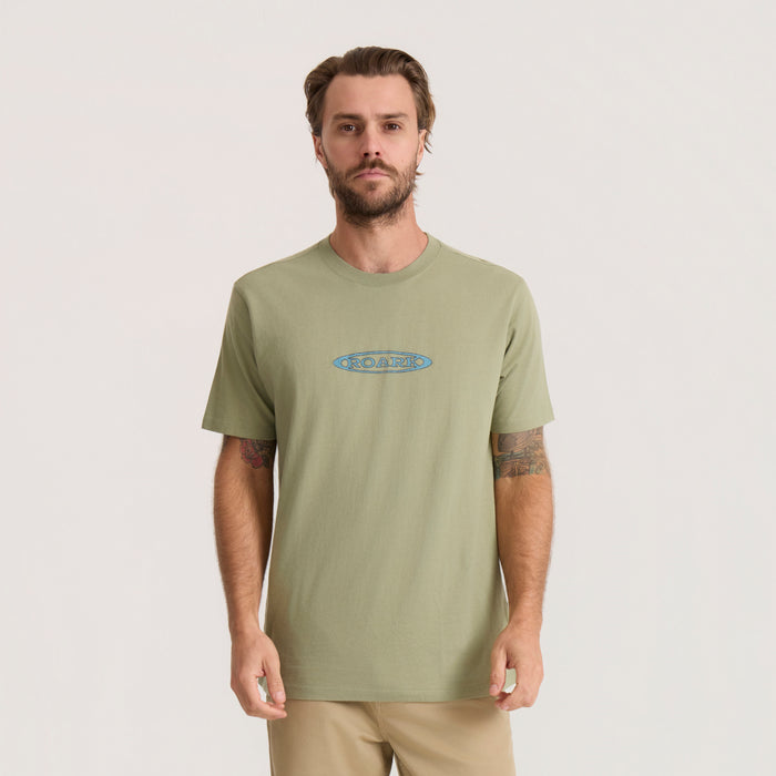 Sage green Roark Moto Premium Tee with blue embroidered logo, worn by man with tattoos on neutral background