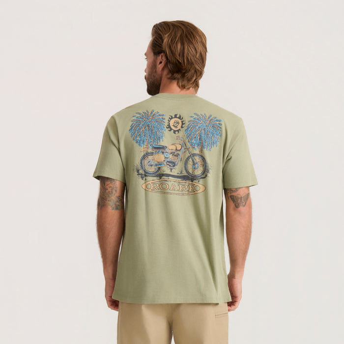 Sage green Moto Premium Tee worn by man showing back print of motorcycle, palm trees, sun and Roark branding