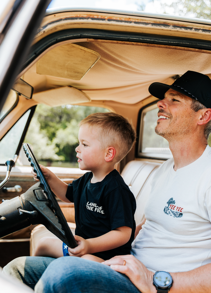 Man and child sitting in a car, with the child holding a toy steering wheel.