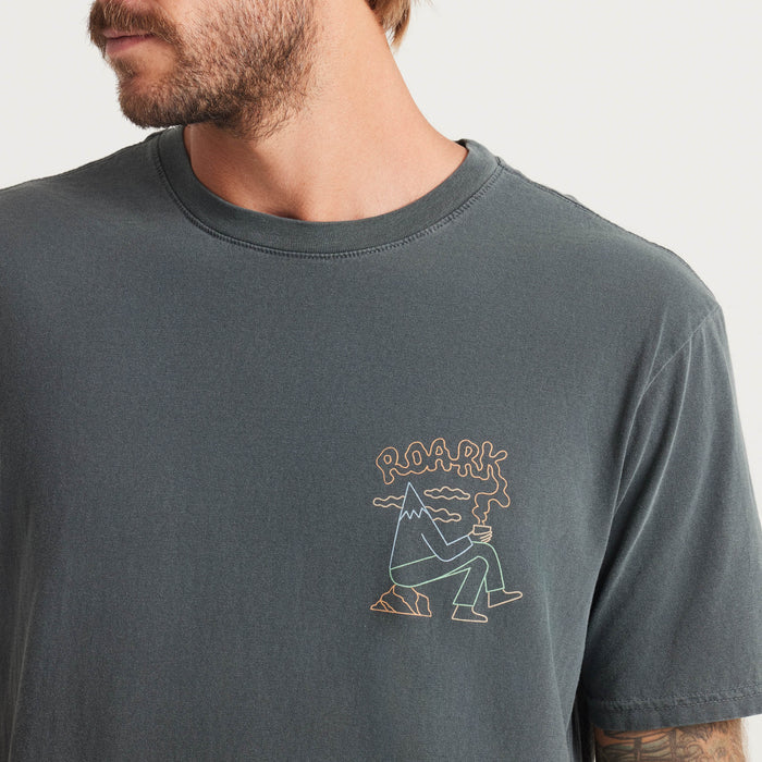 A man dons a blue Roark t-shirt with colorful graphics, embodying an adventurous spirit and casual style, perfect for outdoor enthusiasts.