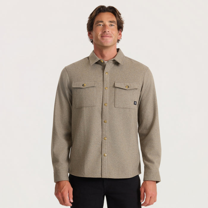 Man wearing tan long-sleeve flannel shirt with chest pockets and metal buttons over black pants against white background