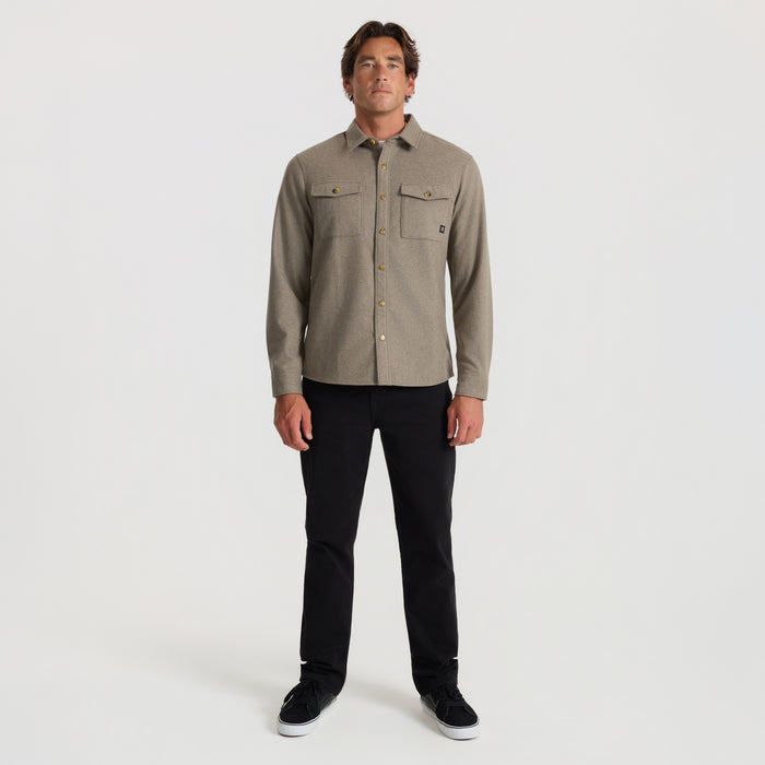 Man wearing dusty green flannel shirt with dual chest pockets and gold buttons, styled with black jeans and black sneakers