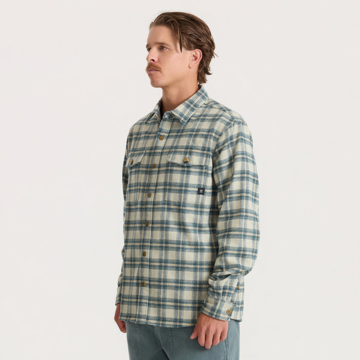 Man wearing Nordsman 2.0 long sleeve flannel in sand with blue plaid pattern and button front, styled with gray jeans