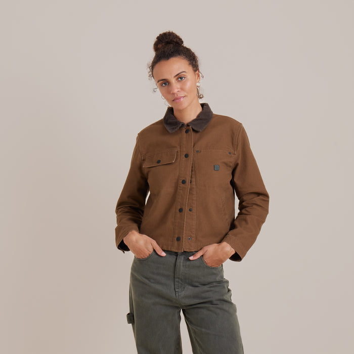 Rustic scene featuring a Roark Open Road canvas jacket with button details, displayed against a backdrop of sorrel and livestock, evoking a sense of adventure and outdoor travel.