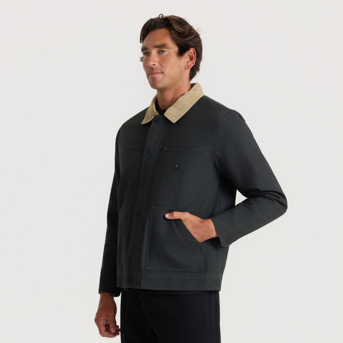 Black waxed canvas jacket with tan collar worn by man standing against neutral background