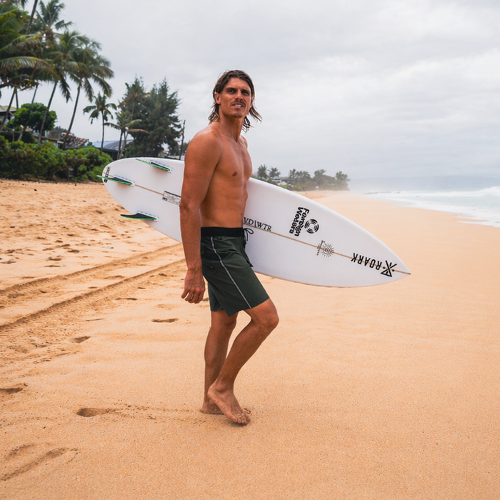 Surfer with surfboard walking on an empty sandy beach, embodying the spirit of adventure and solitude in Roark's exploration lifestyle.