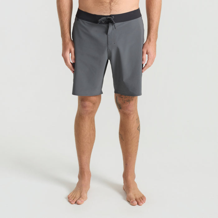 Rugged outcrop and serene lake in the Lake District, featuring a barechested man in Roark boardshorts embodying adventure and the call of the wild.