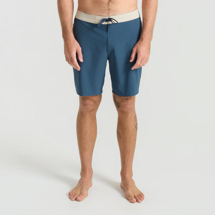 Surfer wearing navy Bermuda boardshorts while surfing in the ocean, embodying Roark's adventurous and travel-inspired outdoor lifestyle.