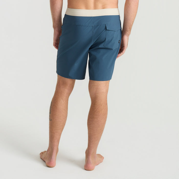 Roark boardshorts in navy blue styled casually on sandy beach, evoking a sense of adventure and relaxation.