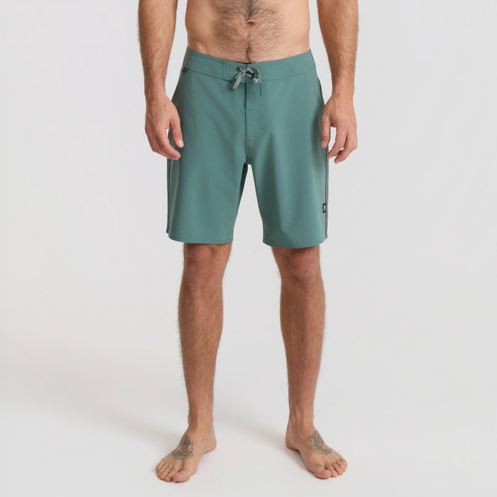 Man wearing boardshorts wading into the ocean on a sunny beach vacation, embodying the spirit of adventure.