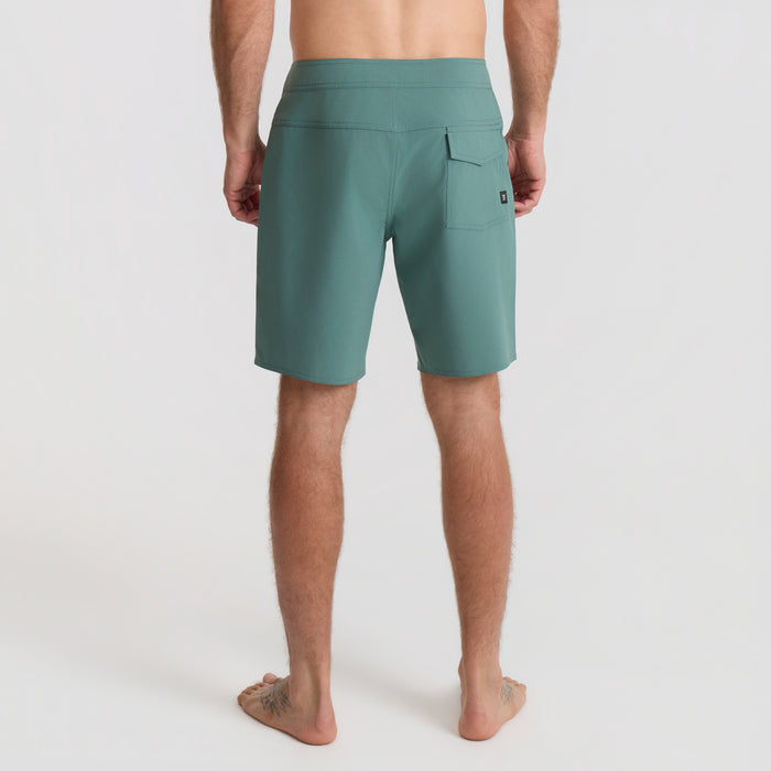 Adventurous person lounging in tropical setting wearing Bermuda boardshorts, embodying Roark's spirit of travel and outdoor leisure.