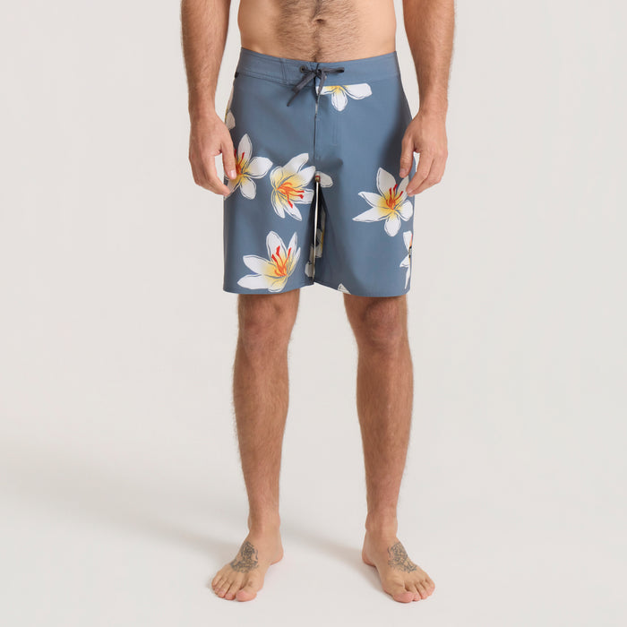 Blue board shorts with white and yellow floral print, drawstring waist, displayed on male model barefoot against neutral background