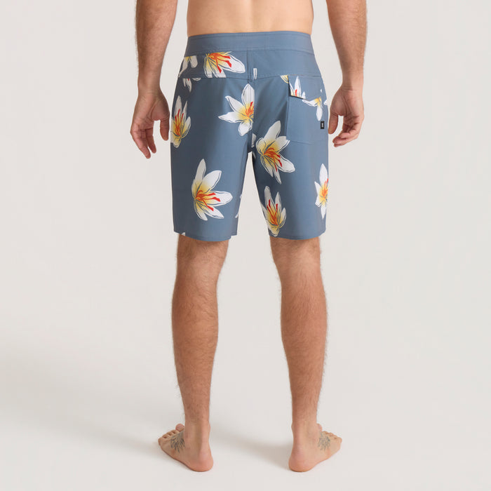 Slate blue boardshorts with white and yellow floral pattern, shown on model from behind, knee-length cut