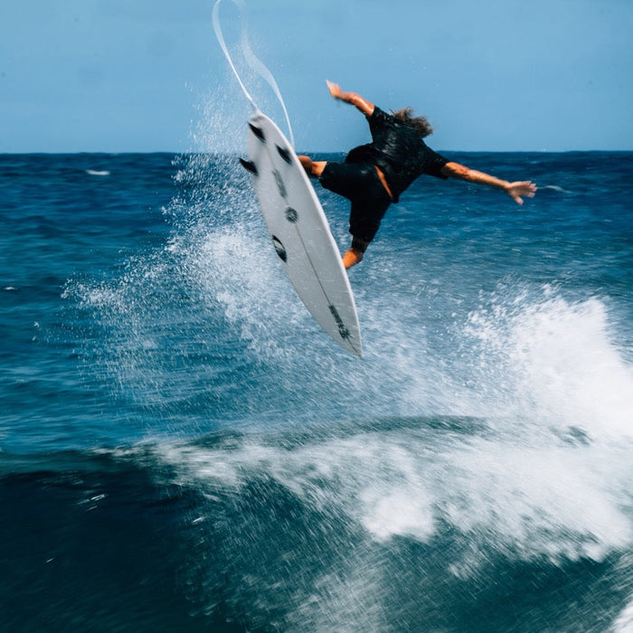 Surfer in black Passage Pro boardshorts kicks out on white surfboard in ocean wave spray