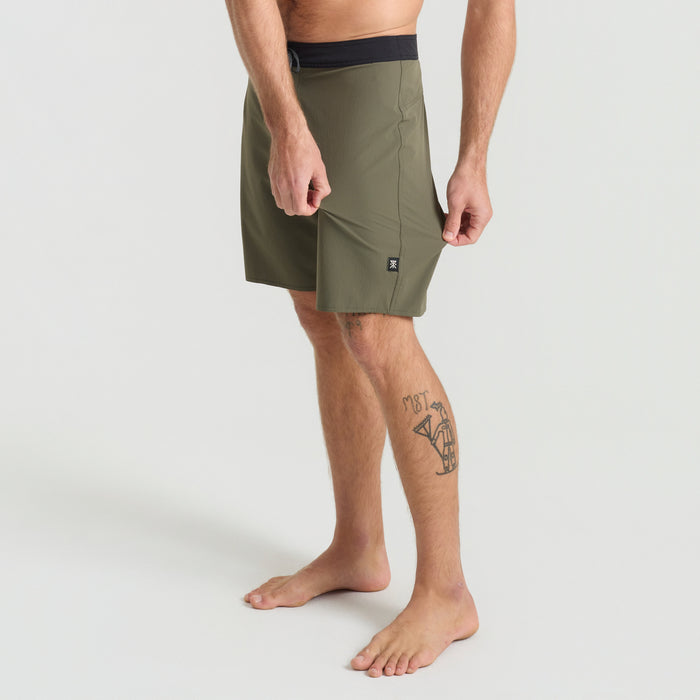 Man wearing Roark boardshorts standing casually by the beachside, epitomizing the adventurous spirit of travel and leisure.