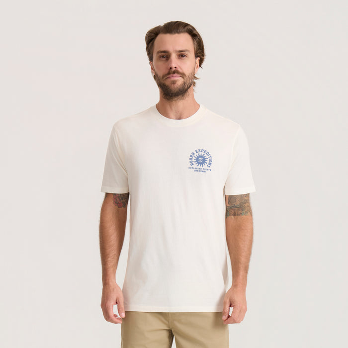 Off white short sleeve t-shirt with blue circular graphic logo on chest, worn by male model with tan pants