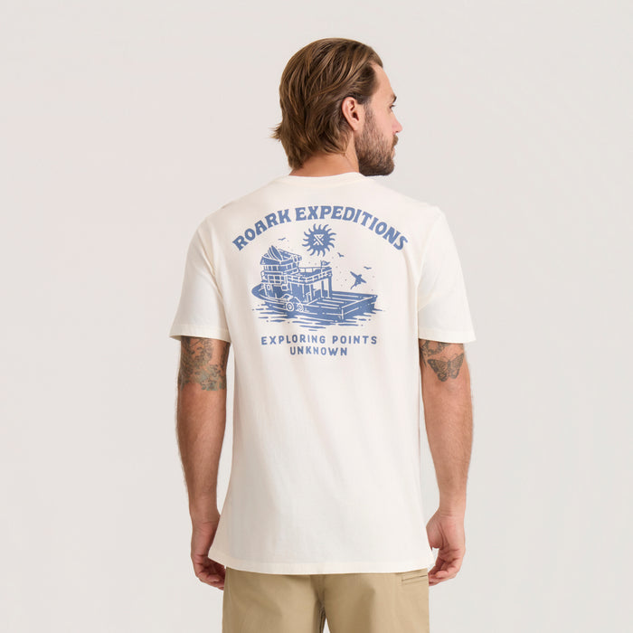 Cream colored short sleeve t-shirt worn by man, featuring blue Roark Expeditions graphic and exploring points unknown text on back